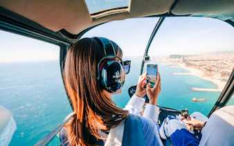 Helicopter passenger photographing coastal city view during shared panoramic tour.