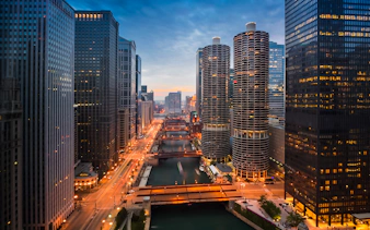 Chicago River at sunset with city skyline and illuminated buildings.