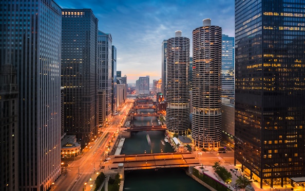Chicago River at sunset with city skyline and illuminated buildings.