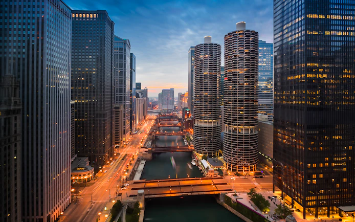 Chicago River at sunset with city skyline and illuminated buildings.