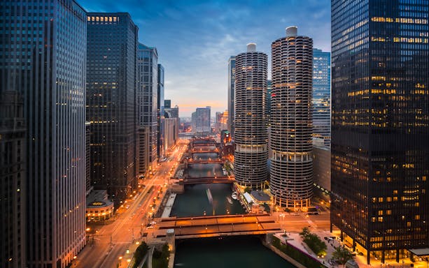 Chicago River at sunset with city skyline and illuminated buildings.
