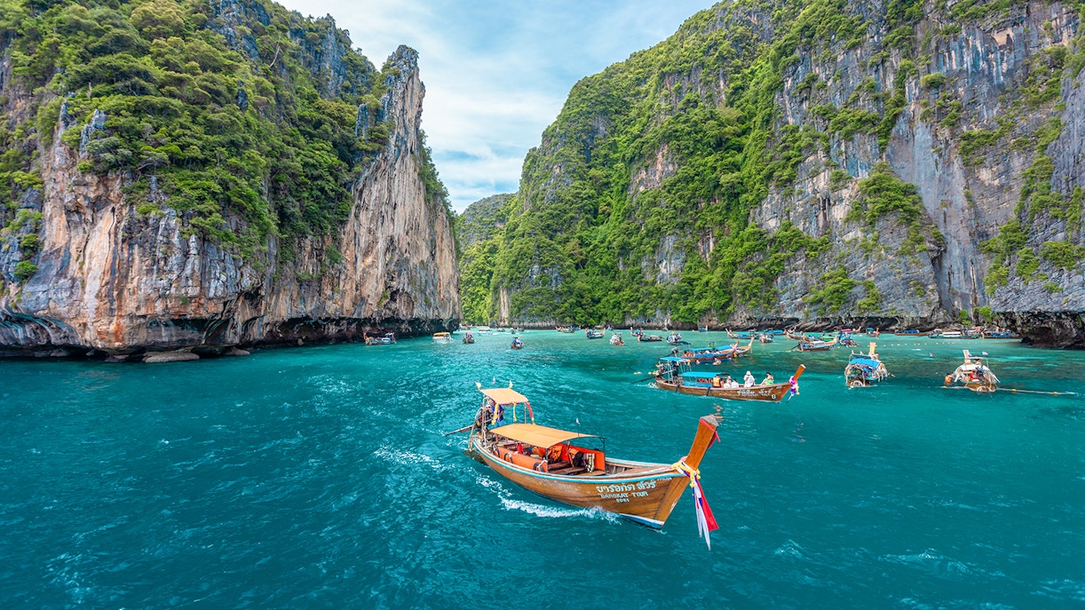 Long-tailed boat in Pileh Lagoon, Phi Phi Islands, Thailand, surrounded by turquoise waters and limestone cliffs.