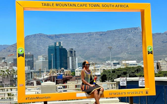Person sitting in a yellow frame with Table Mountain in the background, Cape Town.
