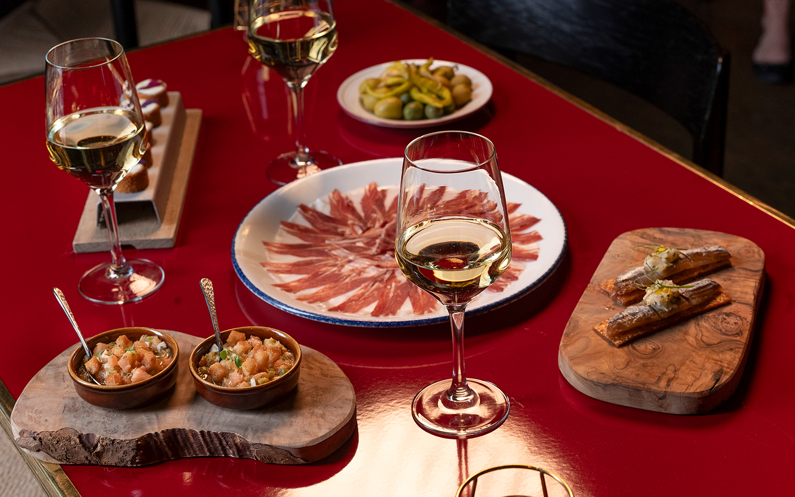 Flamenco De Leones Show tapas with wine, featuring cured ham, olives, and appetizers on a red table.