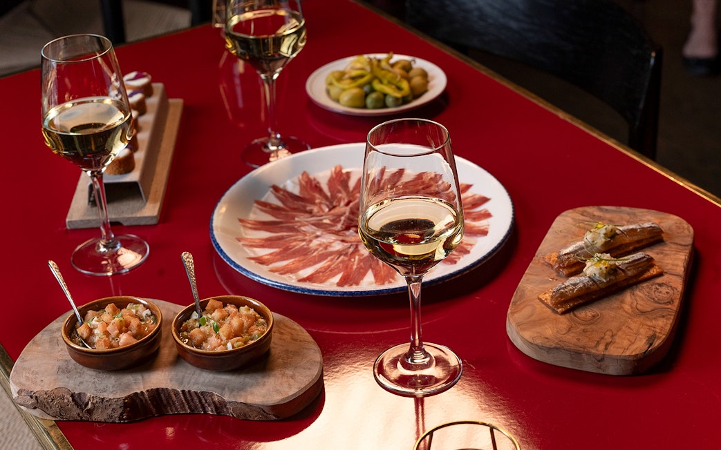 Flamenco De Leones Show tapas with wine, featuring cured ham, olives, and appetizers on a red table.