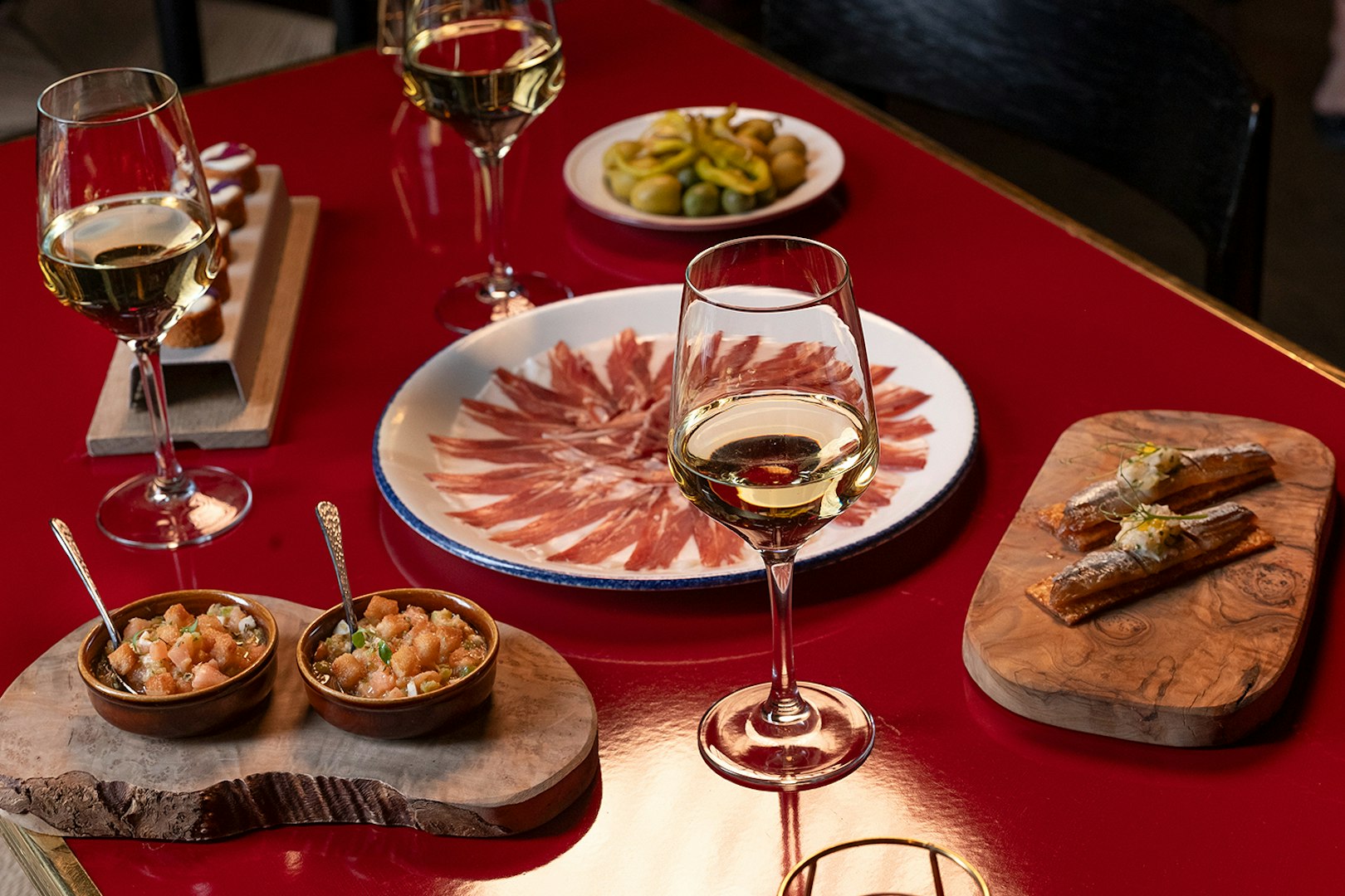 Flamenco De Leones Show tapas with wine, featuring cured ham, olives, and appetizers on a red table.