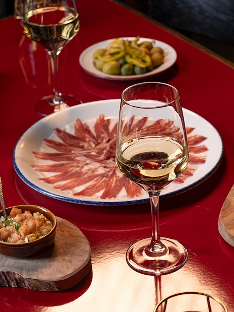 Flamenco De Leones Show tapas with wine, featuring cured ham, olives, and appetizers on a red table.