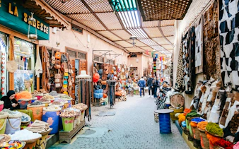 Marrakech souk with colorful textiles, spices, and leather goods on display.