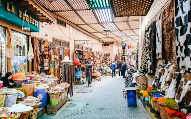Marrakech souk with colorful textiles, spices, and leather goods on display.
