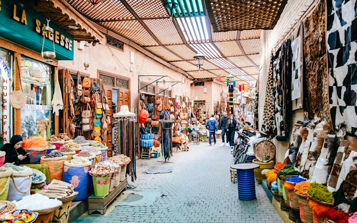 Marrakech souk with colorful textiles, spices, and leather goods on display.