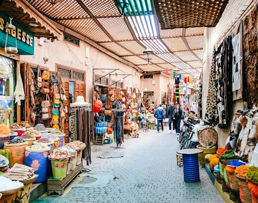Marrakech souk with colorful textiles, spices, and leather goods on display.