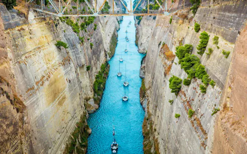Boats navigating the narrow Corinth Canal with steep rock walls, Greece.