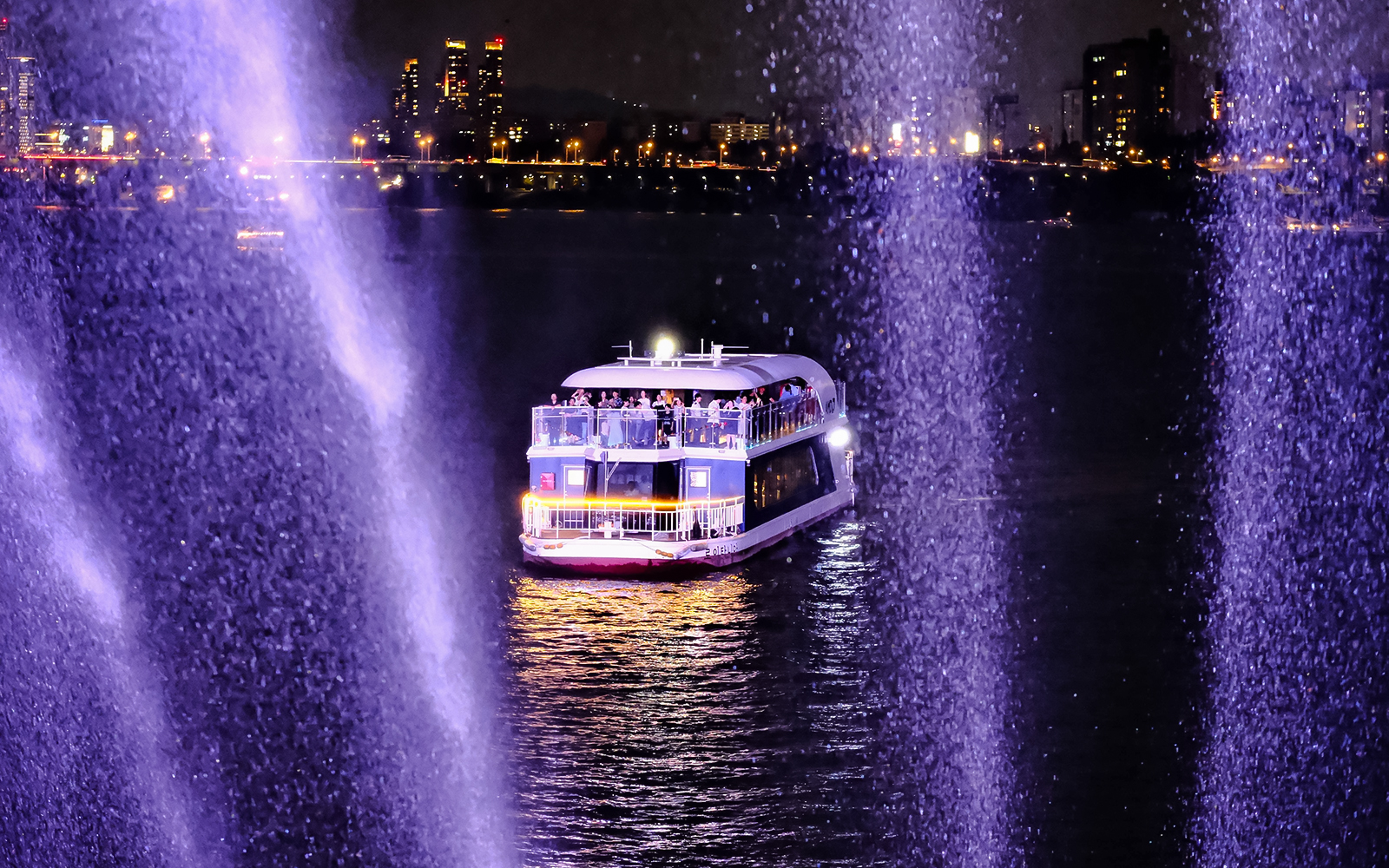 Cruise boat on Han River at night with city lights in the background.