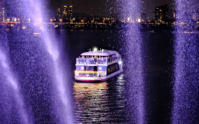 Cruise boat on Han River at night with city lights in the background.