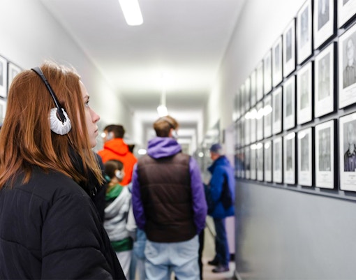 Visitor with audio guide at Auschwitz-Birkenau Memorial, viewing prisoner photos in a hallway.