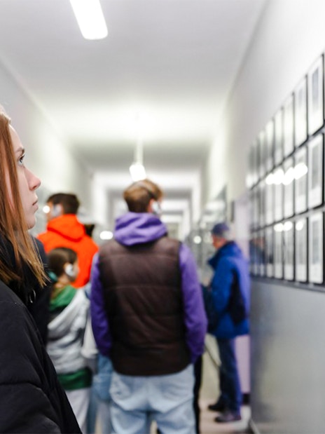 Visitor with audio guide at Auschwitz-Birkenau Memorial, viewing prisoner photos in a hallway.