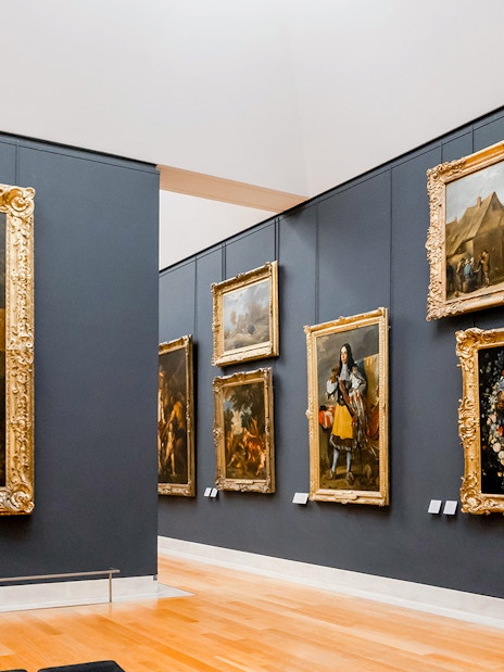 Louvre Museum gallery with classic paintings in ornate frames, Paris.