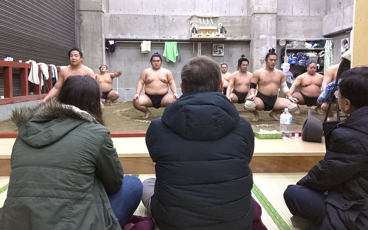Sumo wrestlers training in a Tokyo dojo with spectators watching.