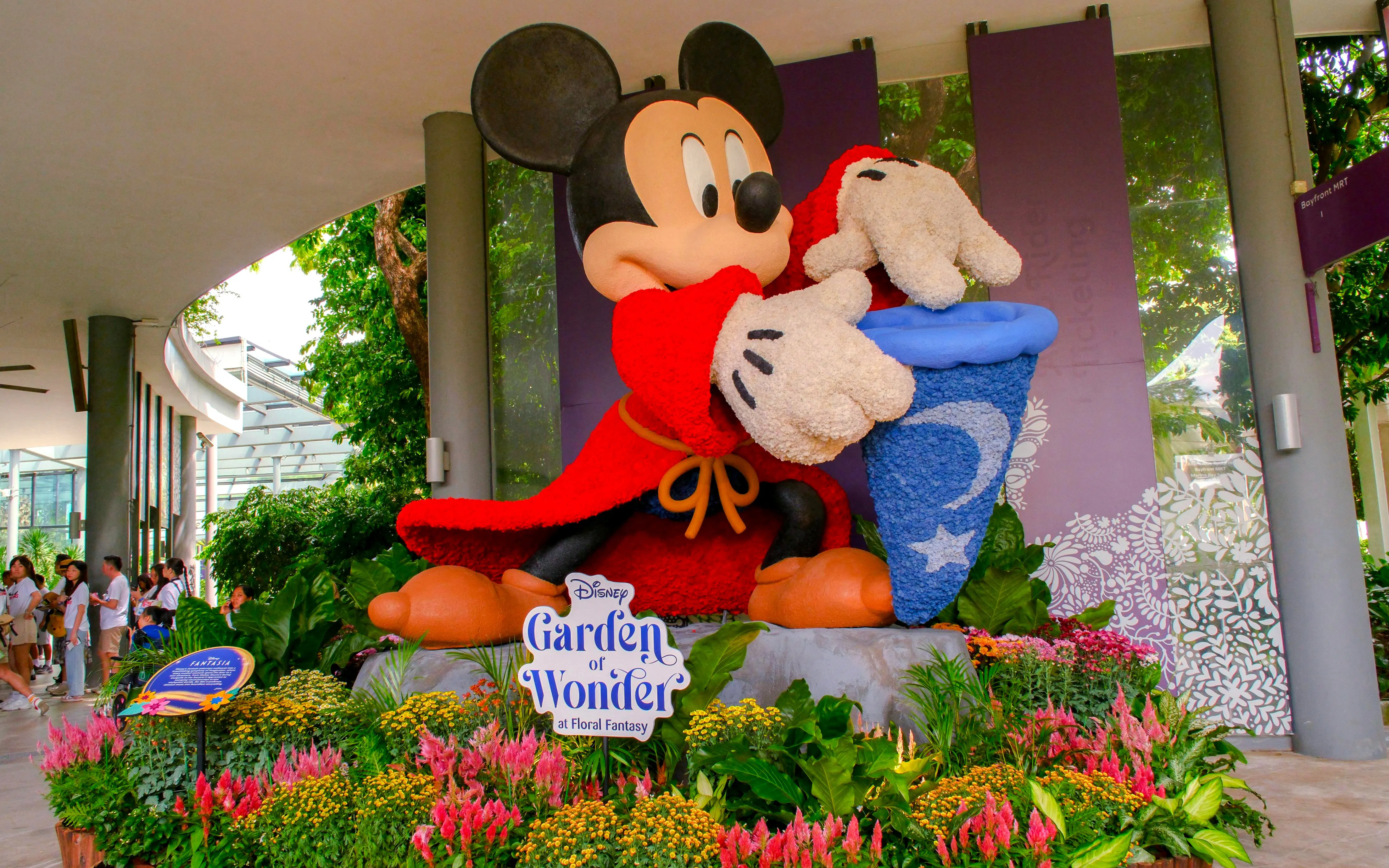 Mickey Mouse statue in red robe at Disney Garden of Wonder, surrounded by colorful flowers.