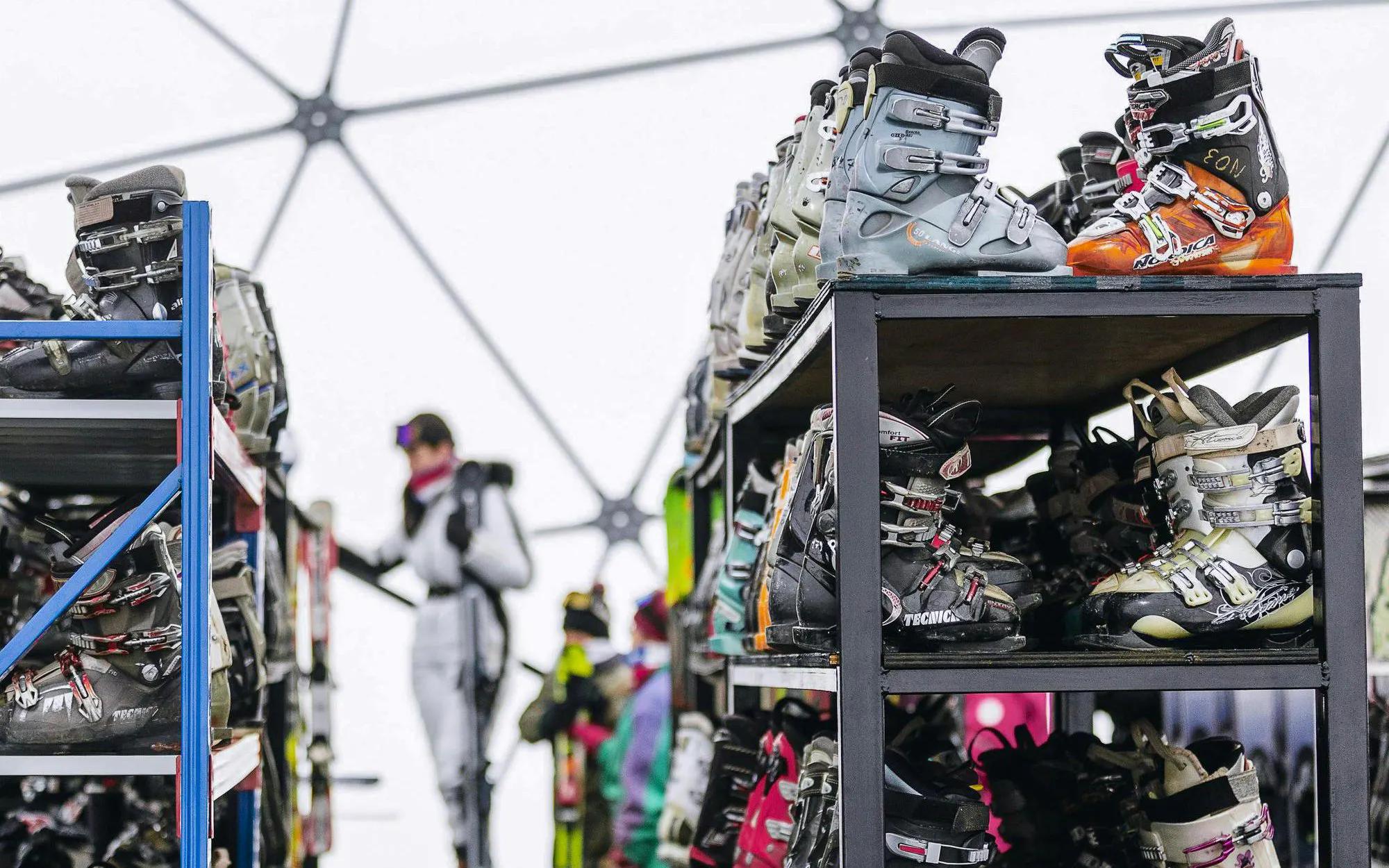 Ski boots on racks at a Chilean ski resort with skiers in the background.