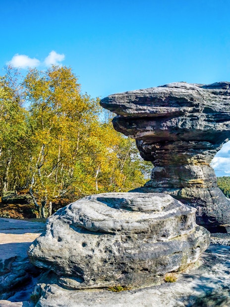Sandstone formations at Tisa Rocks with surrounding forest under a clear blue sky.