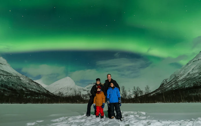 Family under Northern Lights in Tromsø, Norway, with snowy mountains in the background.
