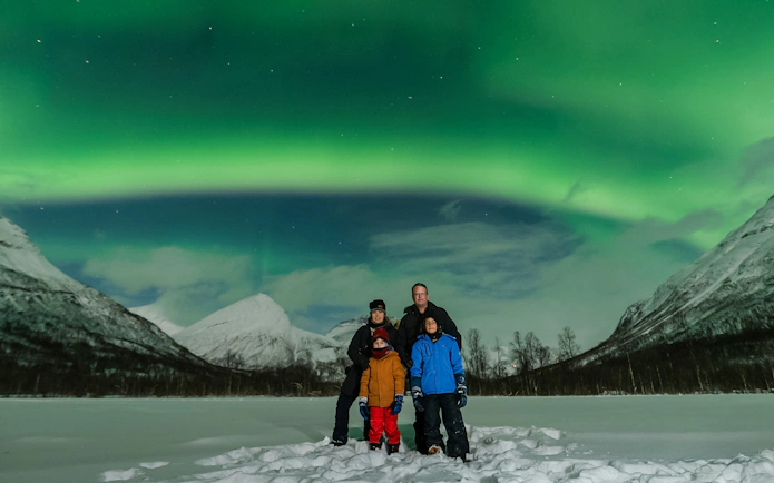 Family under Northern Lights in Tromsø, Norway, with snowy mountains in the background.