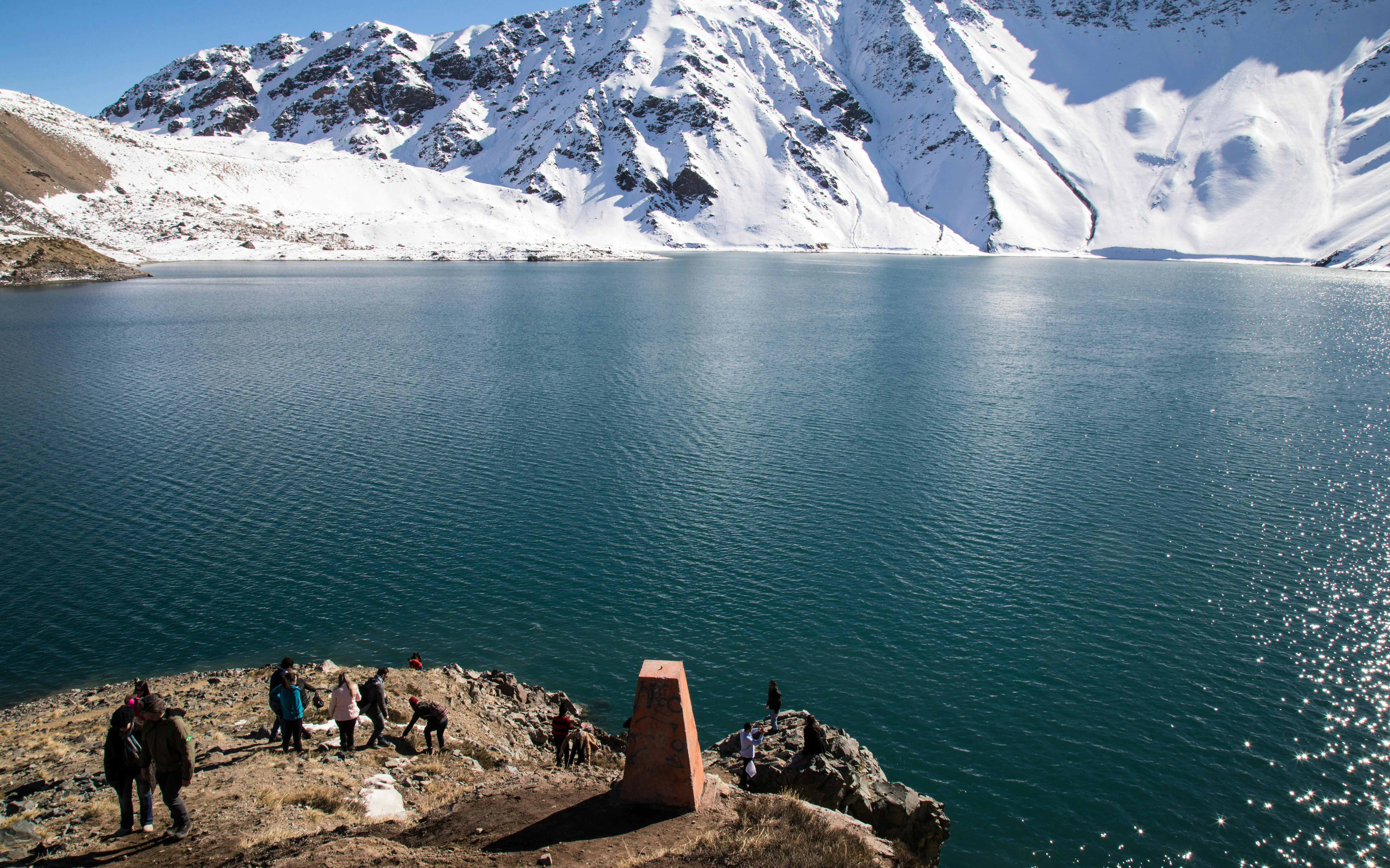 Tourists exploring the shoreline of Embalse El Yeso with snow-capped mountains in the background.