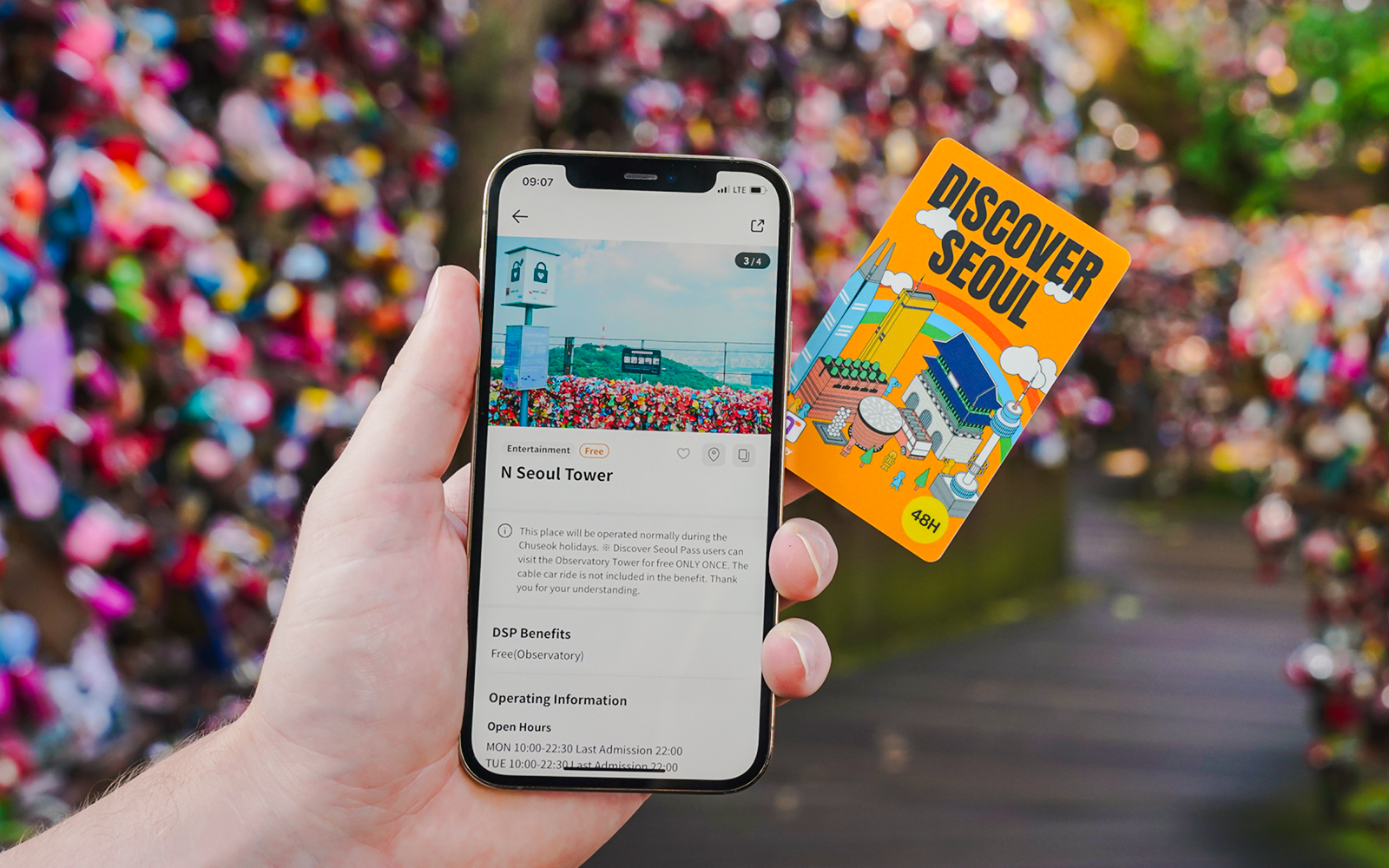 Hand holding a phone displaying N Seoul Tower information and a Discover Seoul pass.