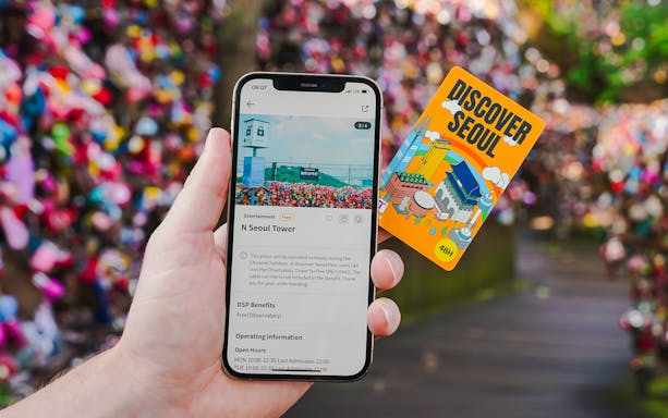 Hand holding a phone displaying N Seoul Tower information and a Discover Seoul pass.