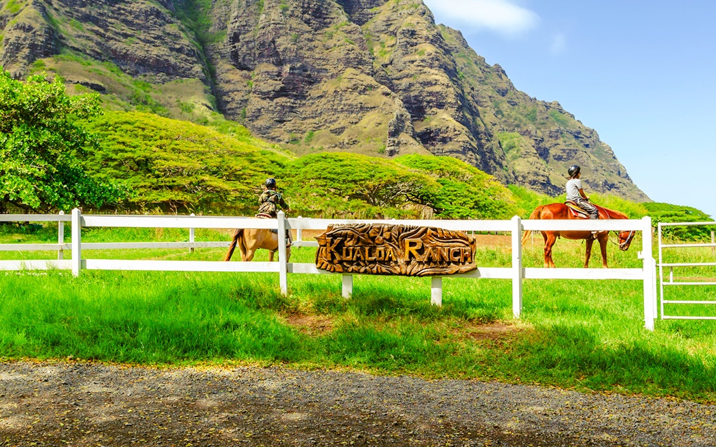 Horseback riders at Kualoa Ranch with lush mountains in Hawaii.