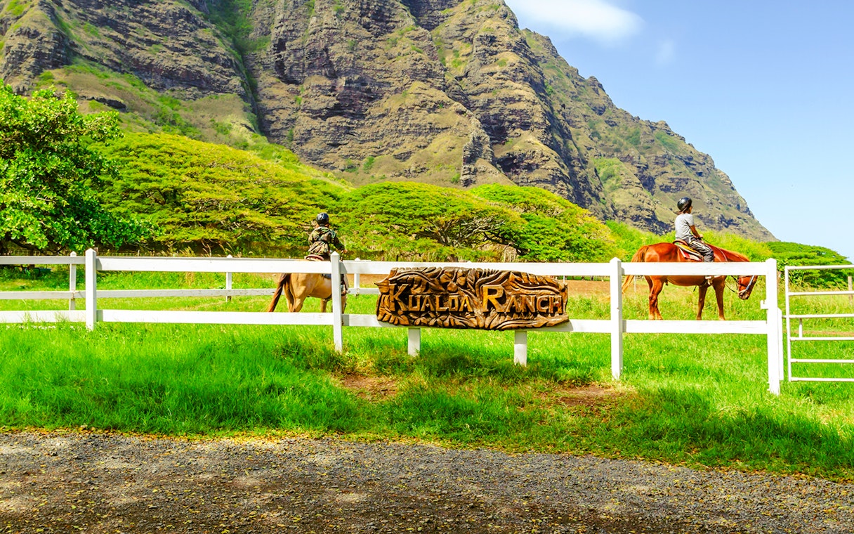 Horseback riders at Kualoa Ranch with lush mountains in Hawaii.