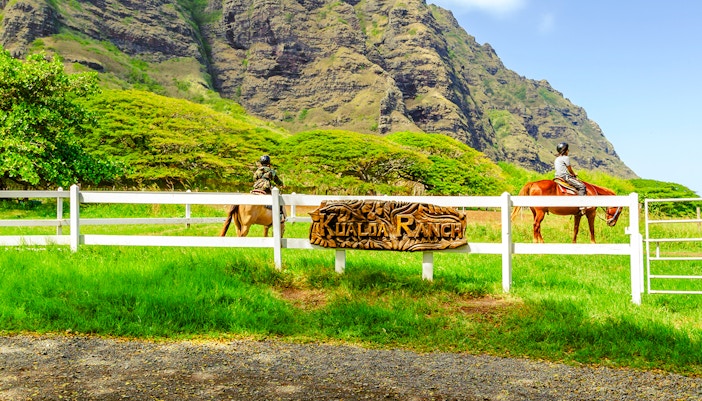 Horseback riders at Kualoa Ranch with lush mountains in Hawaii.