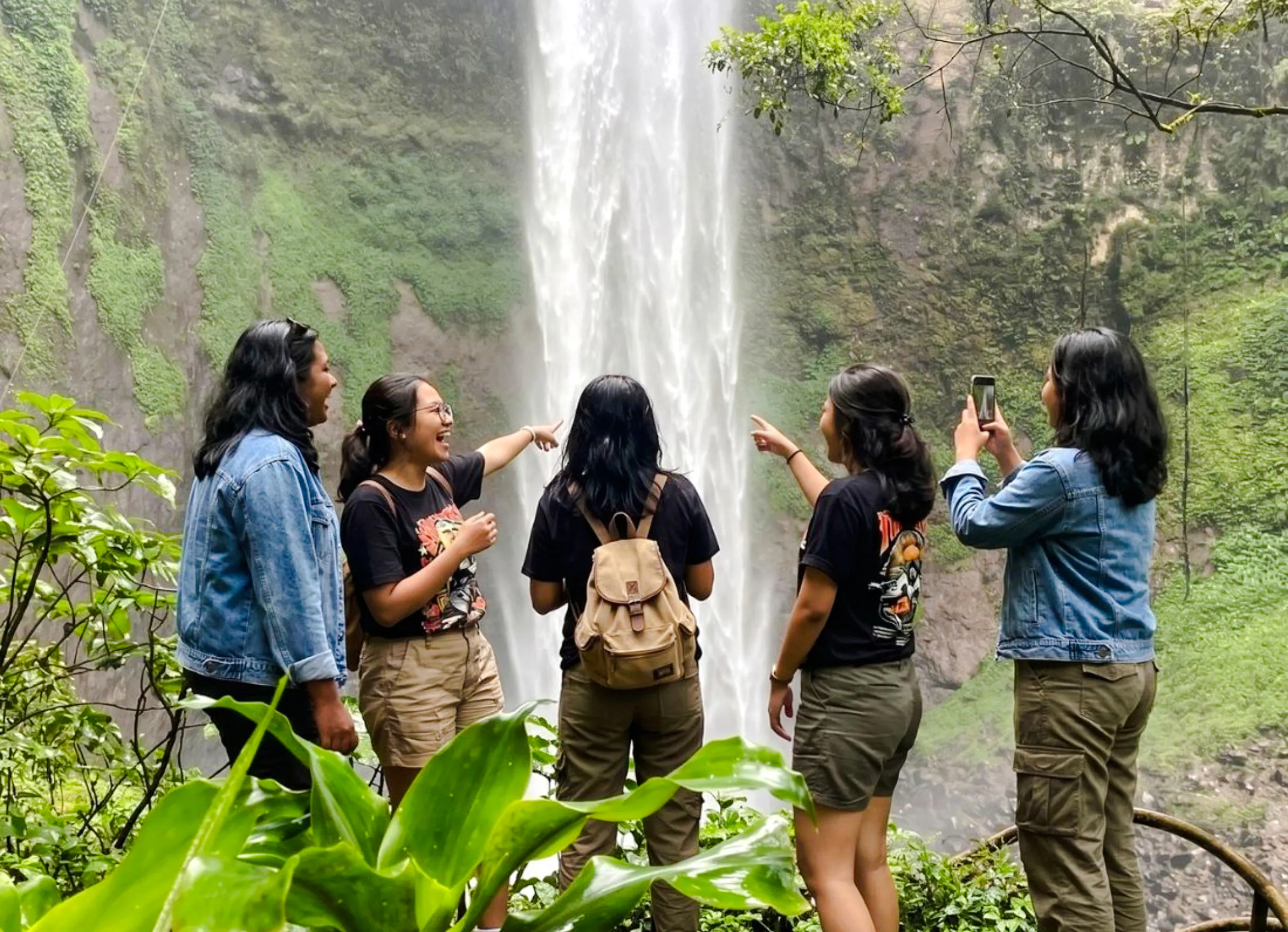 Visitors enjoying Rainbow Waterfall in Bandung, capturing photos and pointing at the cascade.