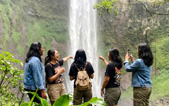 Visitors enjoying Rainbow Waterfall in Bandung, capturing photos and pointing at the cascade.