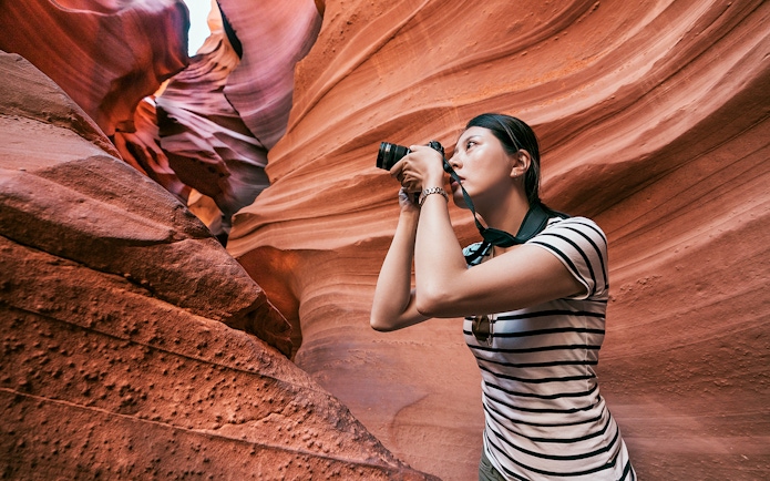 Woman photographing sandstone formations in Upper Antelope Canyon, Arizona.