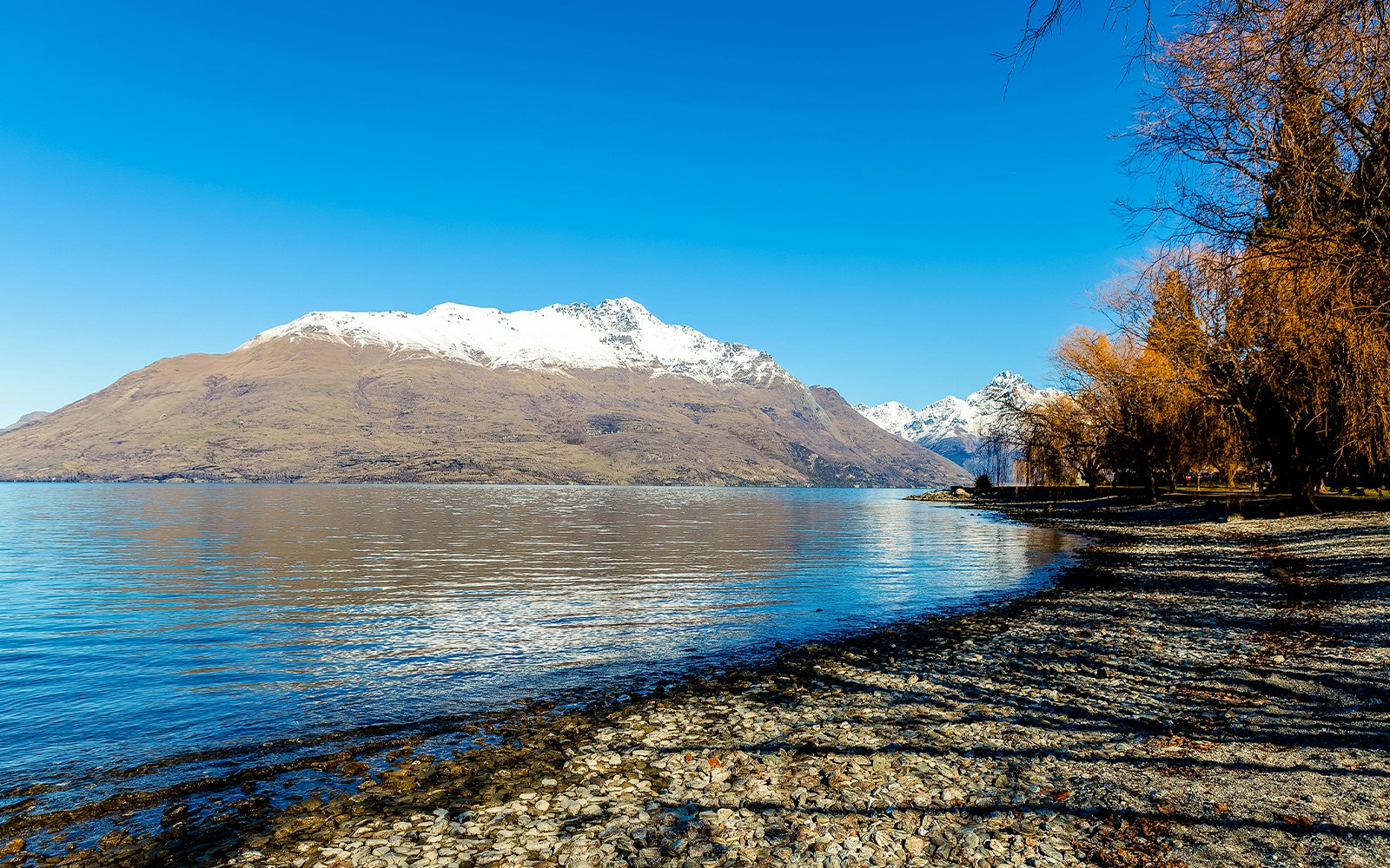 Snow-capped Cecil Peak and The Ledge viewed from Lake Wakatipu's shore in winter.