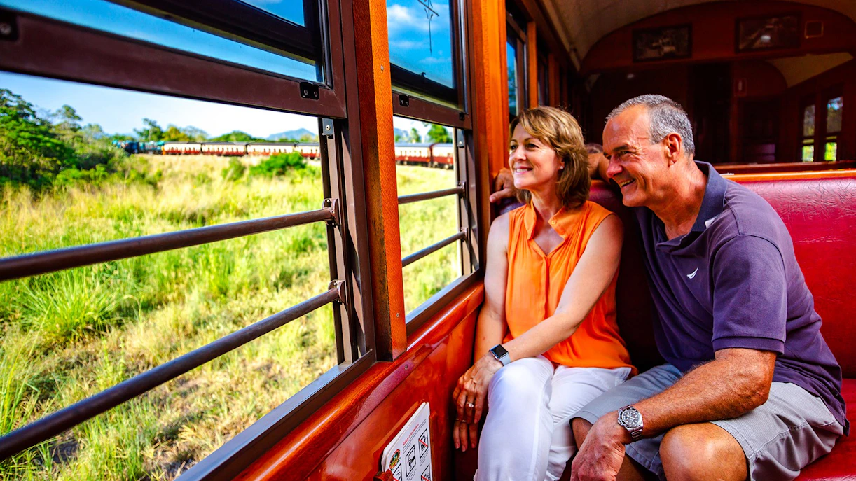 Couple enjoying scenic train ride through Kuranda rainforest near Cairns.