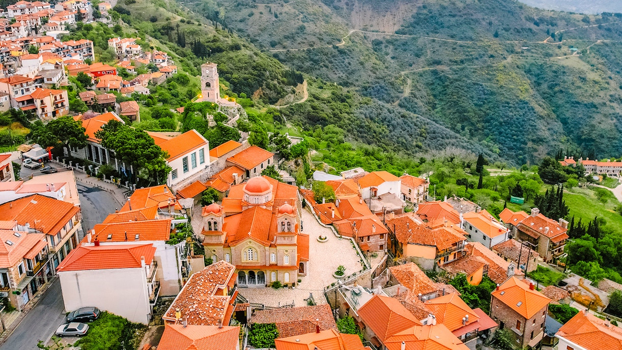 Aerial view of Arachova Village with red-roofed buildings and surrounding green hills.