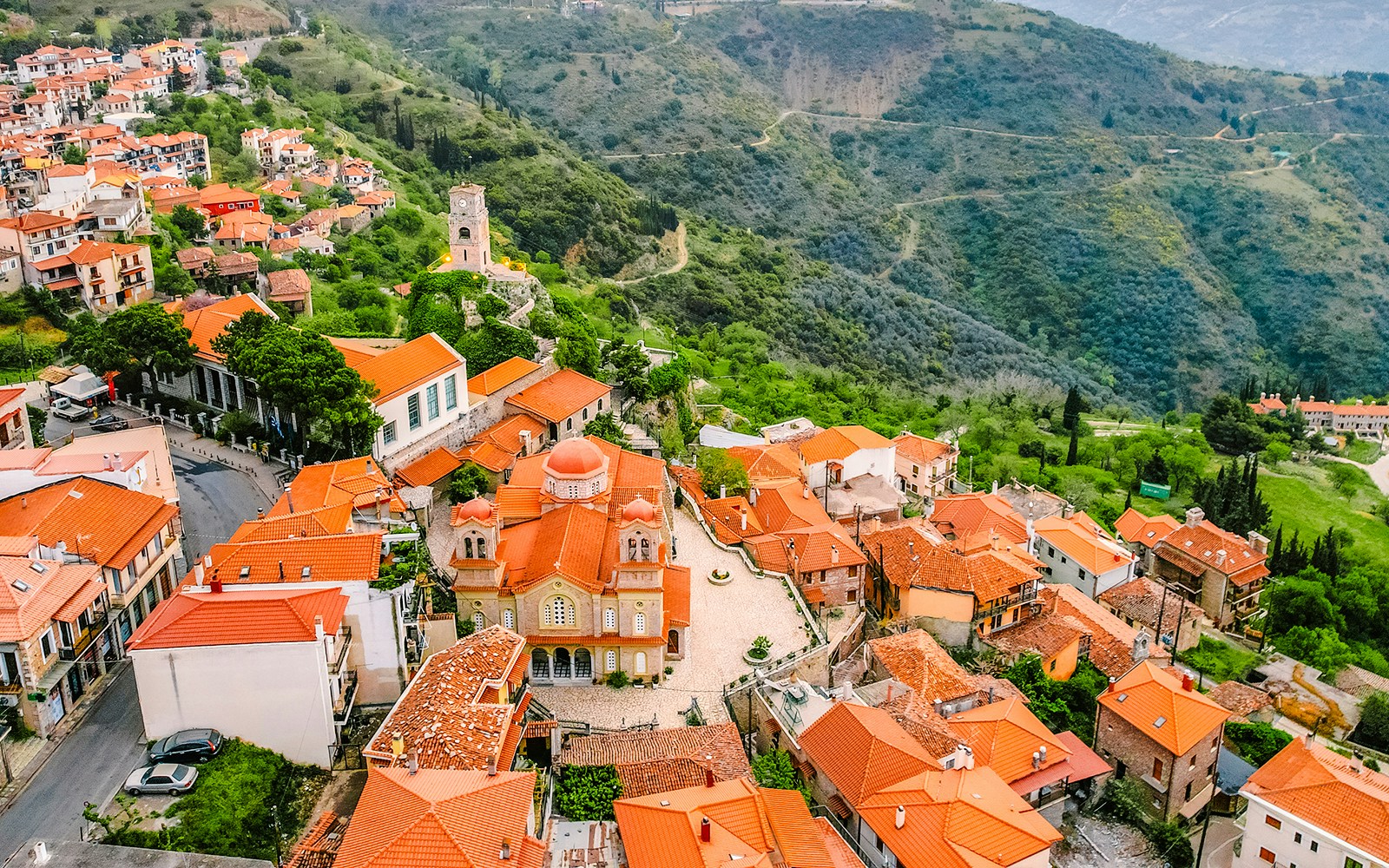 Aerial view of Arachova Village with red-roofed buildings and surrounding green hills.