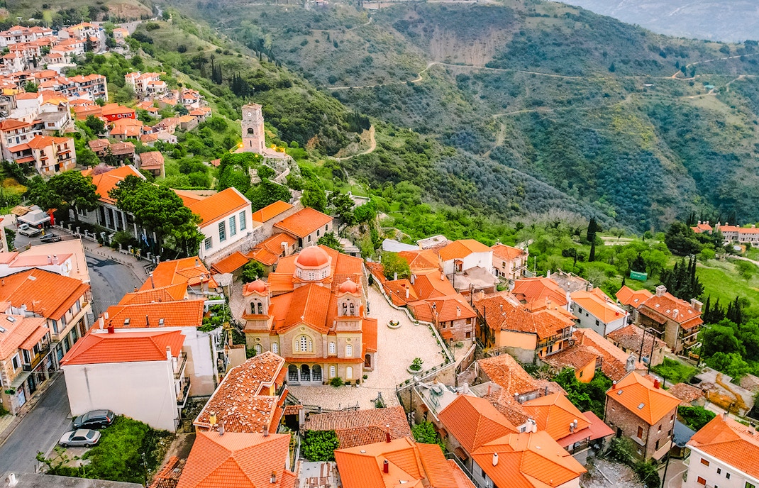 Aerial view of Arachova Village with red-roofed buildings and surrounding green hills.