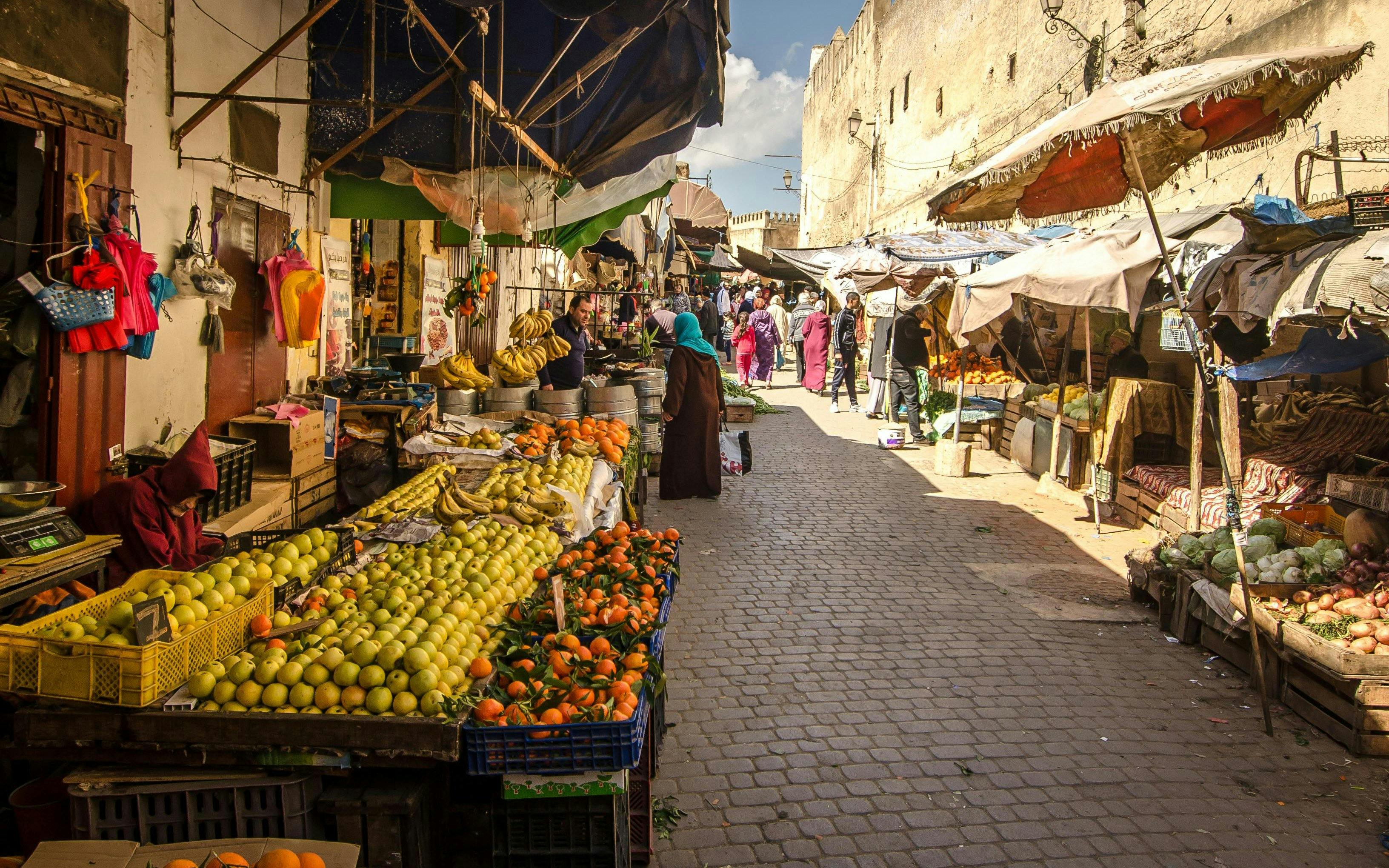 Market stalls with fruits and vegetables in a bustling street in Fez, Morocco.