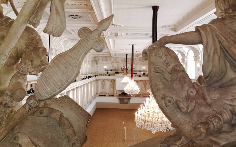 Interior view of the Spanish Riding School arena in Vienna with chandeliers and ornate statues.