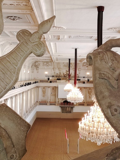 Interior view of the Spanish Riding School arena in Vienna with chandeliers and ornate statues.