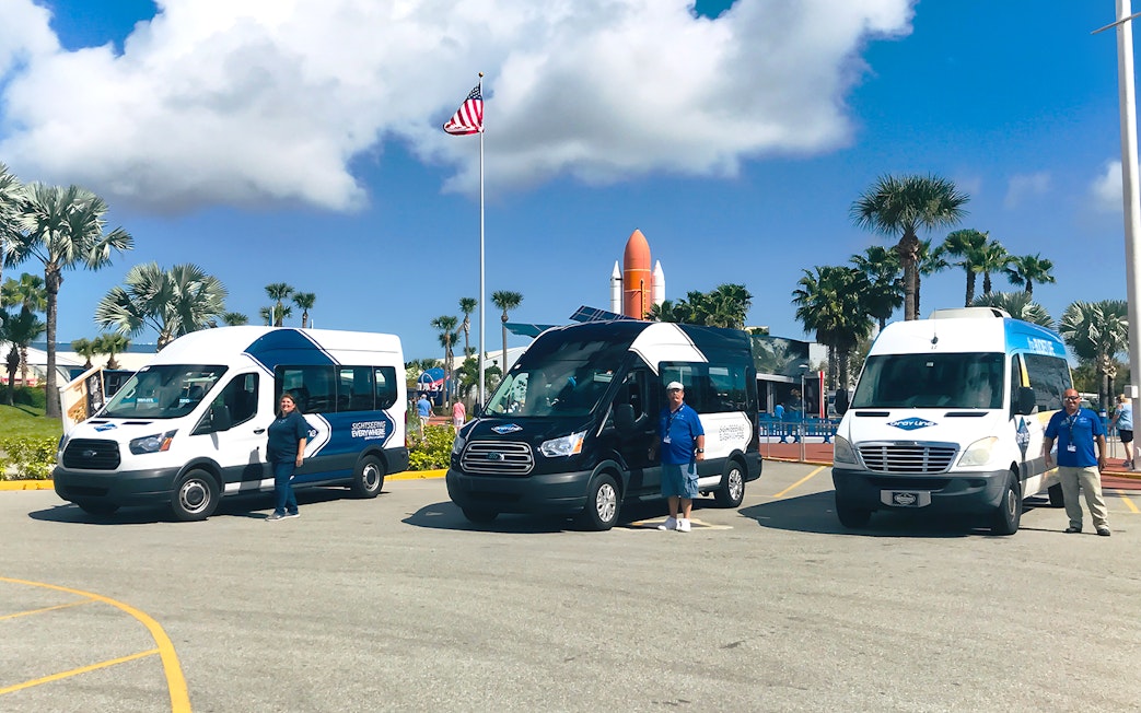 Shuttle vans for transfers to Kennedy Space Center with staff in front.