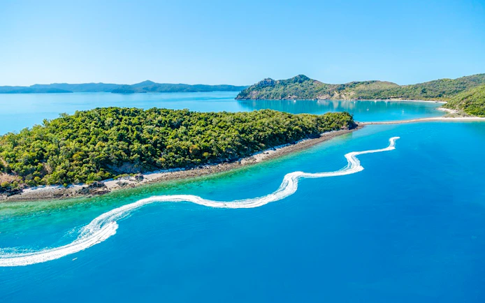 Aerial view of jetski trails near lush island in Whitsundays, Australia.