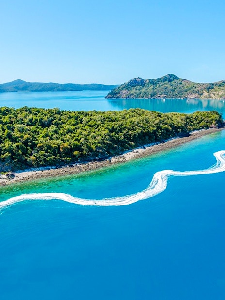 Aerial view of jetski trails near lush island in Whitsundays, Australia.