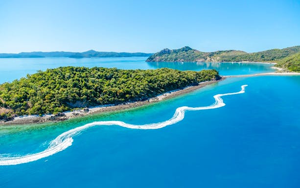 Aerial view of jetski trails near lush island in Whitsundays, Australia.