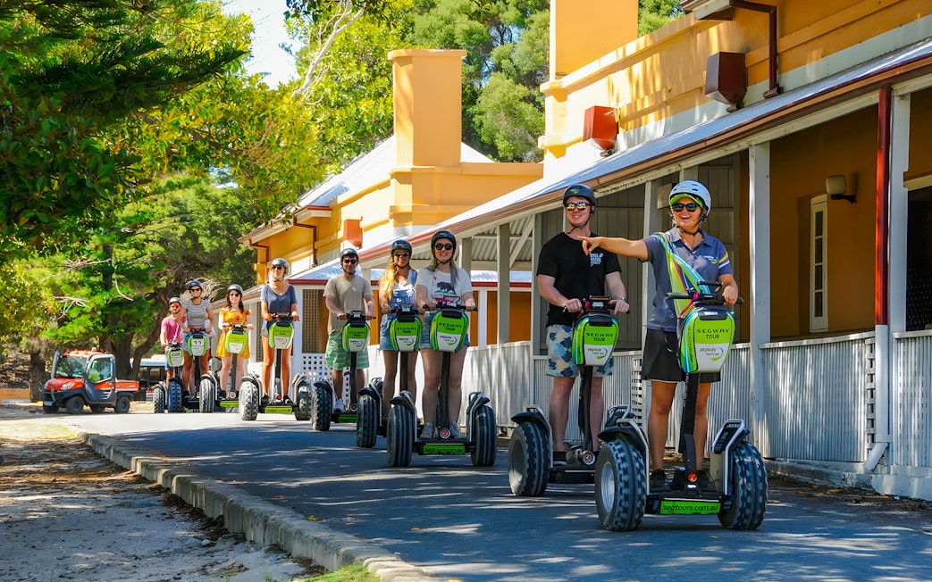 People on Segways during a tour on Rottnest Island, passing historic buildings.