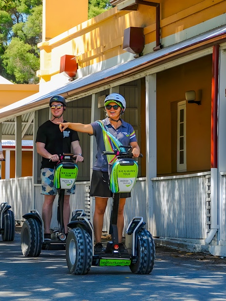 People on Segways during a tour on Rottnest Island, passing historic buildings.